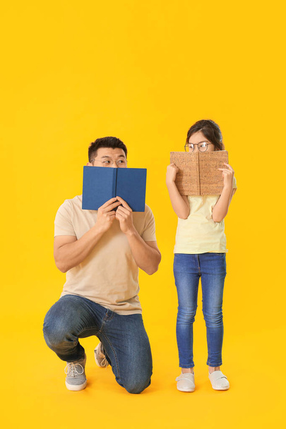 Asian man and his little daughter reading books on color background - Foto, immagini