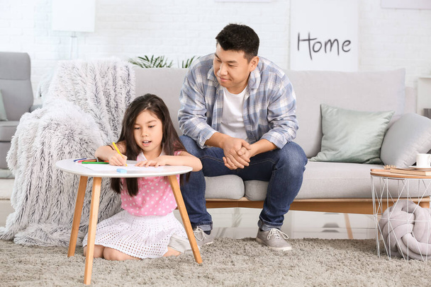 Aasialainen mies katselee pientä tytärtään, joka piirtää kotona
 - Valokuva, kuva