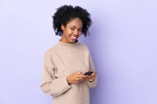 Junge afrikanisch-amerikanische Frau isoliert auf lila Hintergrund senden eine Nachricht mit dem Handy - Foto, Bild