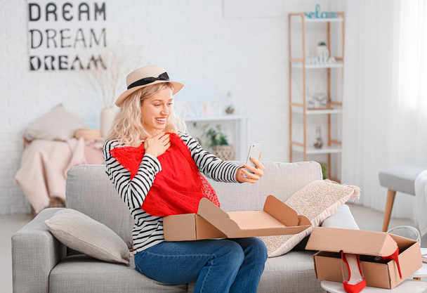 Ευτυχισμένη νεαρή γυναίκα ξεπακετάρισμα κουτί με νέα ρούχα στο σπίτι - Φωτογραφία, εικόνα