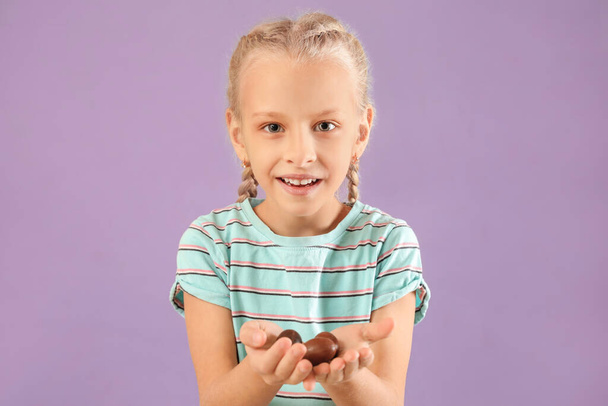 Cute little girl with sweet chocolate eggs on color background - Фото, зображення