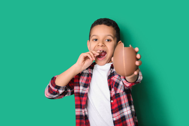 Cute African-American boy with sweet chocolate egg on color background - Photo, image