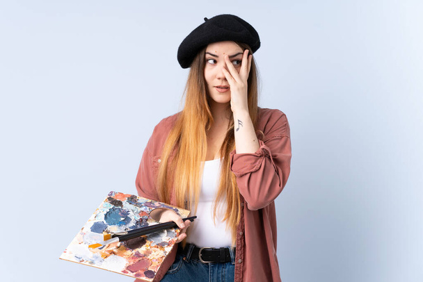 Giovane artista donna tenendo una tavolozza isolata su sfondo blu che copre gli occhi e guardando attraverso le dita
 - Foto, immagini