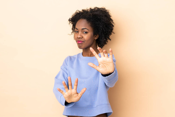 Молодая афроамериканка, изолированная на бежевом фоне, нервничает, протягивая руки к передней - Фото, изображение