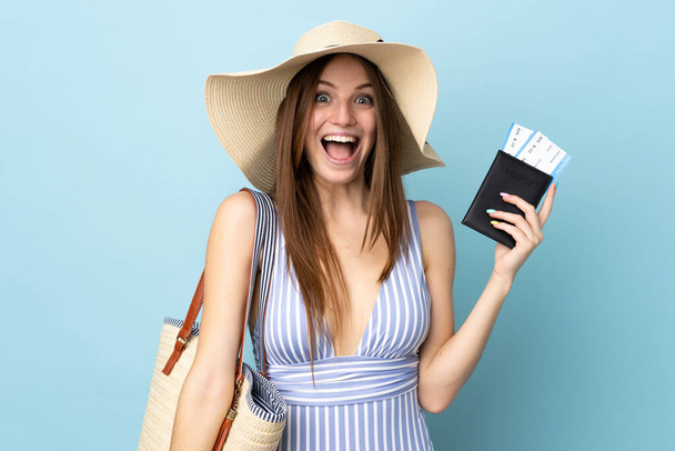 młoda kaukaska kobieta w letnie wakacje posiadające paszport odizolowany na niebieskim tle z zaskoczeniem i wstrząśnięty wyraz twarzy - Zdjęcie, obraz