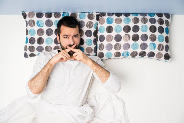 Uomo a letto in vista dall'alto che mostra un segno di silenzio gesto
 - Foto, immagini