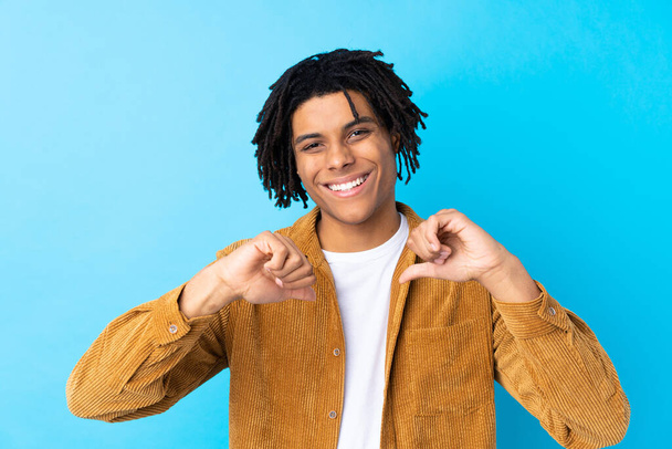 Молодой афроамериканец в вельветовой куртке на изолированном синем фоне гордый и самодовольный
 - Фото, изображение