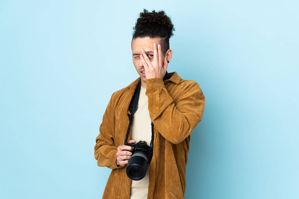 Photographer man over isolated blue background covering eyes and looking through fingers - Foto, immagini