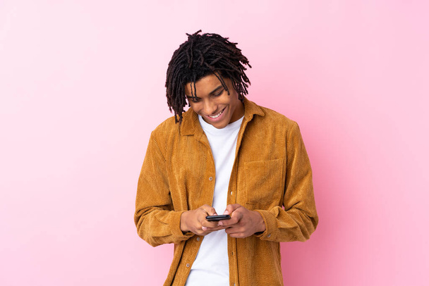 Young African American man with corduroy jacket over isolated pink background sending a message with the mobile - Foto, imagen