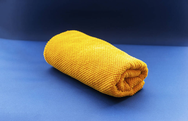 Κίτρινη πετσέτα ισολογισμένη σε μπλε φόντο. - Φωτογραφία, εικόνα