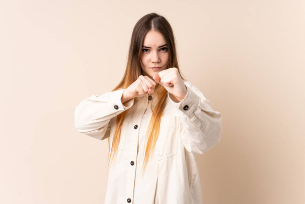 Young caucasian woman isolated on beige background with fighting gesture - Фото, зображення