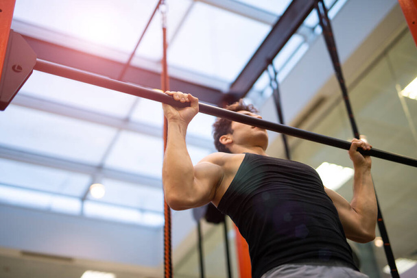 Man doing free body calisthenic pull-ups to taring his back and shoulders in a gym, fitness and bodybuilding concept - Photo, Image