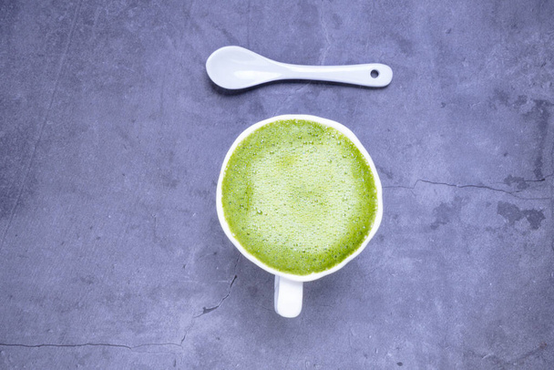 Matcha green tea latte beverage in white ceramic cup with spoon on concrete grey background, top view, copy space - Photo, image