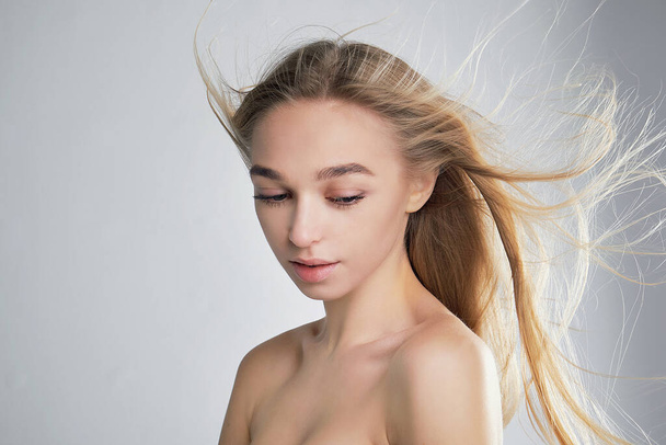 Portrait of a beautiful girl with fluttering hair with wind. Windy hair. Pretty model female look down with perfect fresh clean skin. - Photo, Image