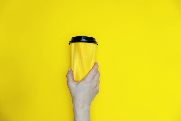 Yellow coffee paper cup in girl hand is on yellow background - Φωτογραφία, εικόνα