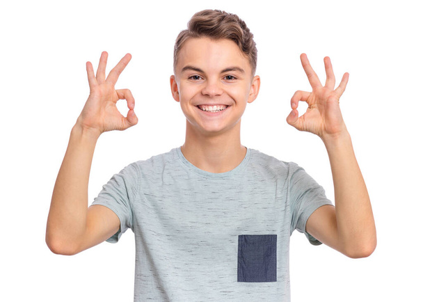 Portrait of teen boy making Ok gesture, isolated on white background. Handsome caucasian young teenager smiling and giving OK sign. Happy cute child showing okay. - Фото, зображення