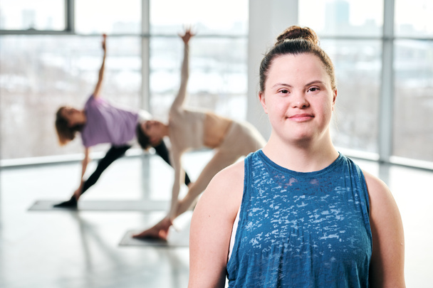 Счастливая молодая инвалидная женщина в спортивной одежде смотрит на тебя после тренировки в спортзале на фоне ее друзей, тренирующихся
 - Фото, изображение