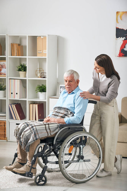 Jovem doador de cuidados femininos conversando com pensionista do sexo masculino de cabelos grisalhos sentado em cadeira de rodas enquanto fica em casa
 - Foto, Imagem