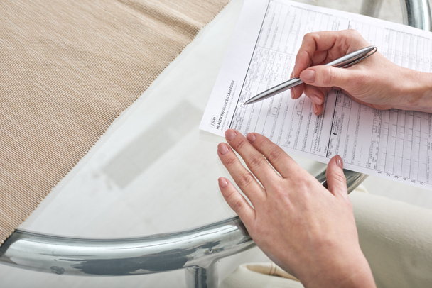 Manos de trabajadora social joven con bolígrafo sobre papel ayudando a su cliente a llenar el formulario de reclamo de seguro de salud
 - Foto, imagen