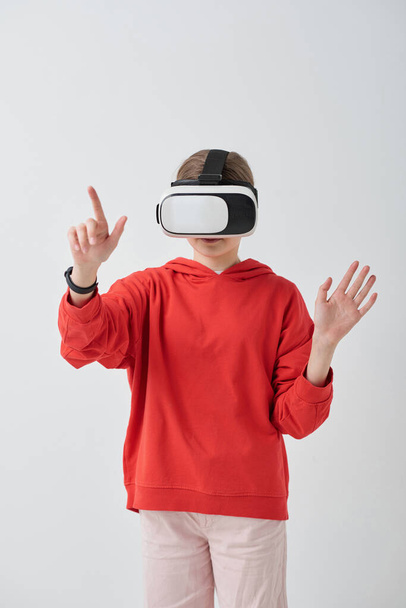 Шкільна дівчина в червоному светрі використовує симулятор віртуальної реальності при вирішенні завдання в освітній відеогрі
 - Фото, зображення