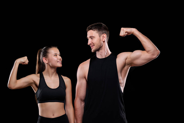 Joven pareja de deportes alegres en ropa deportiva mirándose mientras muestran su fuerza frente a la cámara
 - Foto, Imagen