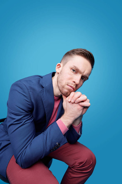 Portrait of pensive young man with beard leaning head on hands against blue background - Foto, afbeelding