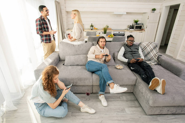 Hoge hoek schot van vijf jonge mannen en vrouwen ontspannen samen in moderne appartement kamer - Foto, afbeelding