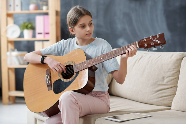 コンテンツ10代の女の子はソファに座って、ギターを学びながらタブレット上でインターネットを使用して - 写真・画像