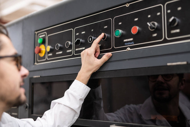 Over schouder zicht van jonge operator drukknop op het bedieningspaneel tijdens het werken in de geautomatiseerde industrie - Foto, afbeelding