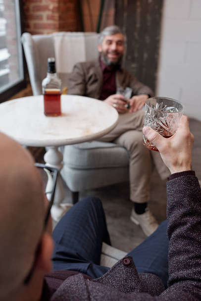 Přes rameno pohled na muže pití drahé whisky s blízkým přítelem v obýváku baru - Fotografie, Obrázek