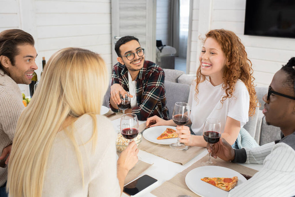 Οριζόντια υψηλής γωνίας πλάνο των νέων ανδρών και γυναικών κουβέντα, ενώ έχοντας το γεύμα στο σύγχρονο διαμέρισμα - Φωτογραφία, εικόνα