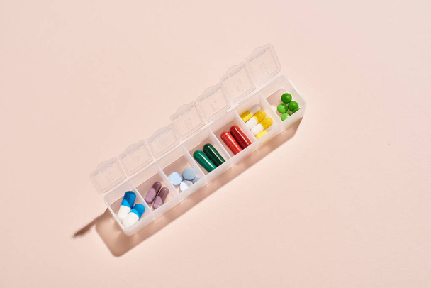 From above horizontal shot of portable plastic container for drugs with medicaments in it on pale pink background - Fotografie, Obrázek