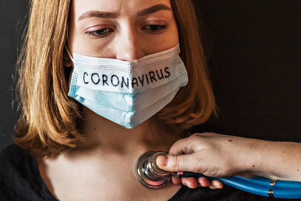 Een close-up portret van een meisje met een ijzig masker op haar gezicht met vermoedelijk coronavirus, dat de dokter met een stethoscoop beluistert. Nieuw Coronavirus-covid-2019. - Foto, afbeelding