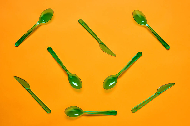 Vízszintes lapos feküdt koncepcionális mintát zöld műanyag kanalakat és villákat élénk narancs alapon - Fotó, kép