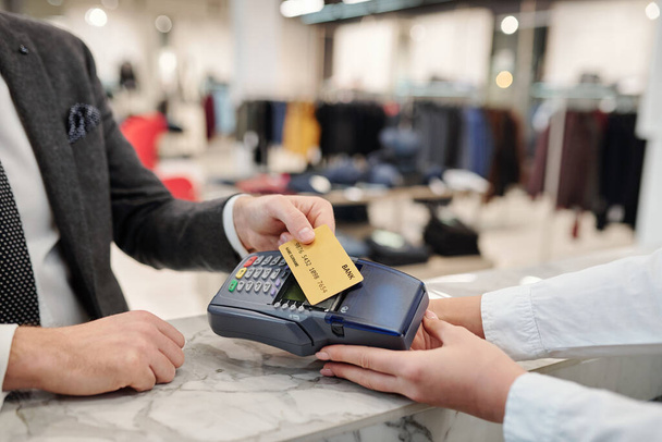 Close-up van onherkenbare zakenman in pak die aan de toonbank staat en met contactloze kaart in de winkel betaalt - Foto, afbeelding
