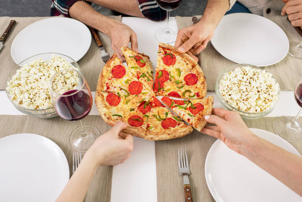 Vízszintes, nagy látószögű felvétel felismerhetetlen emberek kezéről, akik finom pizzaszeleteket fogyasztanak - Fotó, kép