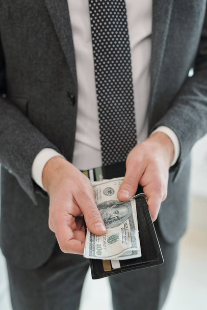 Close-up of unrecognizable businessman in gray suit holding purse and preparing cash for payment - Fotó, kép