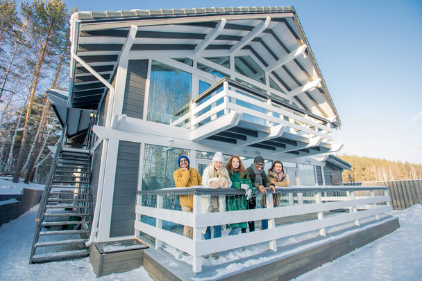 Plan de groupe horizontal de jeunes hommes et femmes vêtus de vêtements d'hiver décontractés debout sur le porche regardant la caméra sourire
 - Photo, image