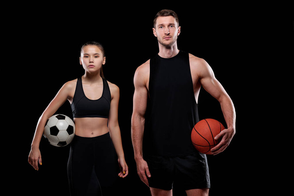 Jonge vrouwelijke voetballer en mannelijke basketballer in sportkleding die ballen vasthoudt terwijl hij voor de camera staat - Foto, afbeelding