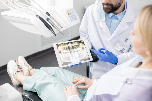 Dentiste professionnel montrant des radiographies dentaires dans le pavé tactile à son patient tout en expliquant ses résultats avant le traitement dentaire
 - Photo, image