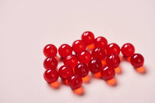 Medicamentos vitamínicos rojos brillantes en la superficie de color rosa pálido, tiro horizontal de cerca
 - Foto, Imagen