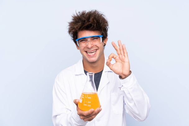 Giovane uomo scientifico su sfondo blu isolato mostrando un segno ok con le dita
 - Foto, immagini
