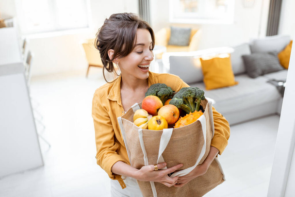 Woman with shopping bag full of fresh food indoors - Fotoğraf, Görsel