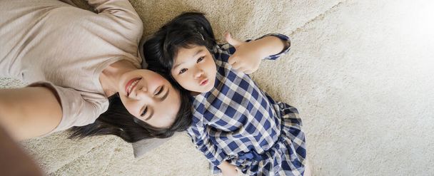happy Asian Family mother and daughter making a fun face selfie photo while lay down on floor use in living room home background. - Foto, Bild