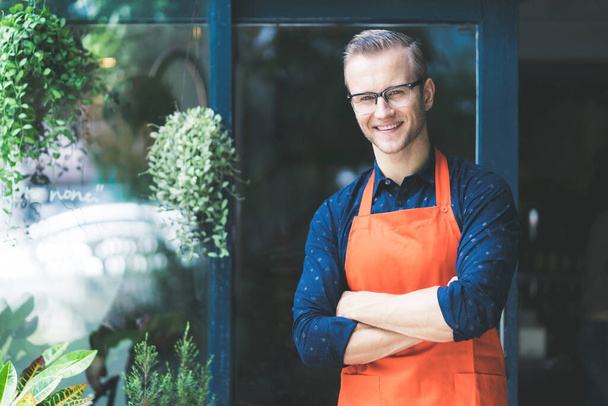 Porträt eines glücklichen jungen Mannes in einer Schürze attraktive kaukasische Male Barista Café Restaurantbesitzer verschränken die Arme und lächeln mit selbstbewusstem und herzlichem Willkommen in seinem erfolgreichen Geschäft - Foto, Bild
