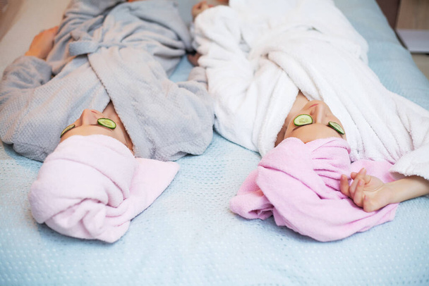 Dvě přítelkyně s ručníky na hlavách, které doma v posteli dělají lázeňské procedury - Fotografie, Obrázek