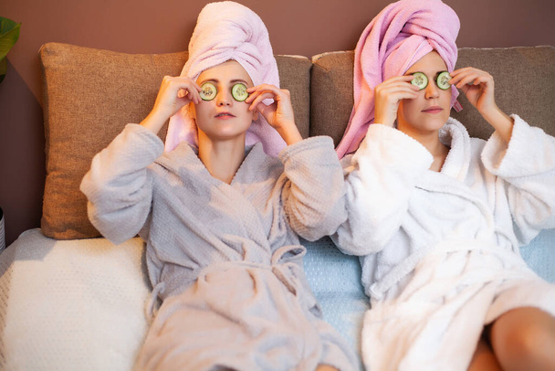 Two girlfriends with towels on their heads, doing spa treatments at home in bed - Photo, Image