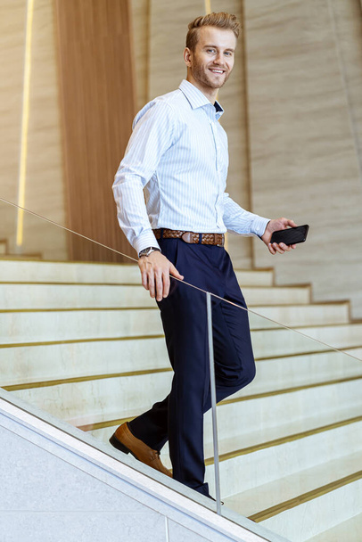 successful smart caucasian businessman walking on stair make communication with smartphone communicate with happiness and enthusiastic modern office background - Zdjęcie, obraz