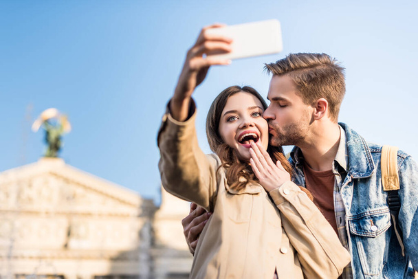 Focus sélectif de l'homme embrasser copine excitée prendre selfie avec smartphone
  - Photo, image