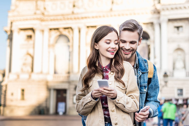 Selective focus of boyfriend and girlfriend smiling with smartphones in city - Photo, Image